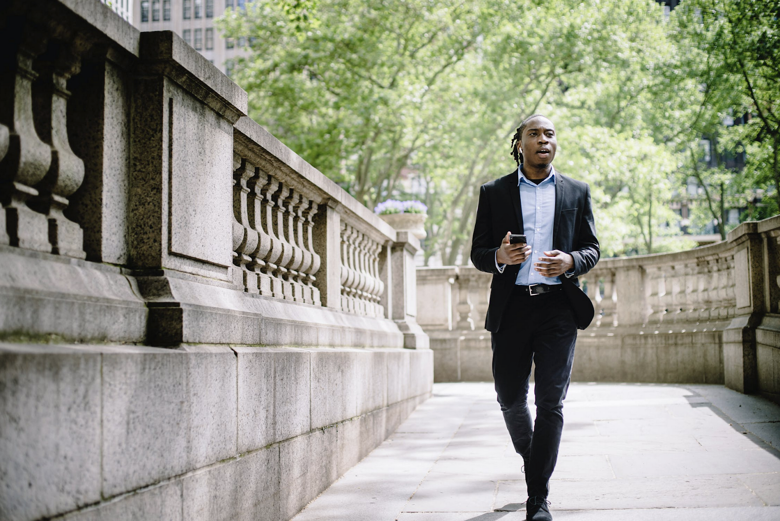 A professional man walking in a city with a smartphone and earbuds.