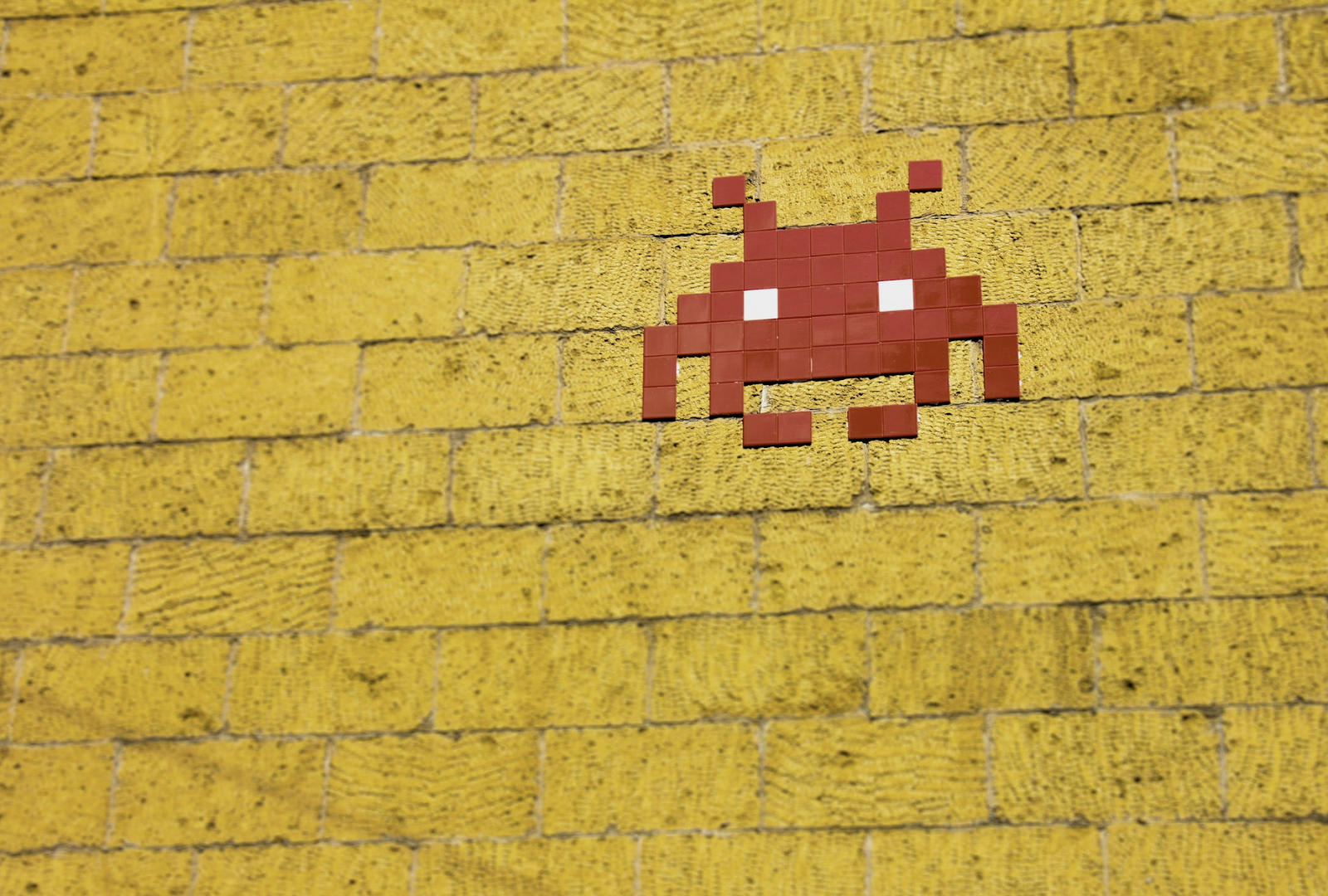 A red pixel alien on a yellow brick background.