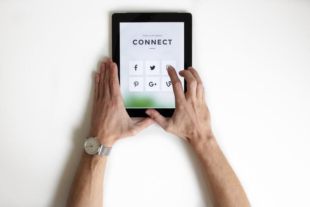 Male arms holding a tablet device showing connections to social media accounts. 